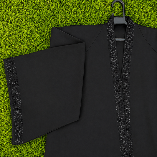 A black traditional robe with wide sleeves and a V-neckline, featuring textured metallic trim along the collar and front opening, displayed on a black hanger over a bright green grass-like background.