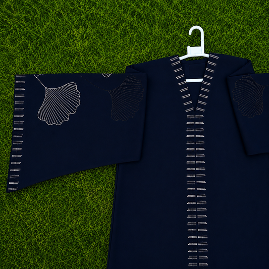 A dark navy kimono-style top with white embroidered details, including a ginkgo leaf motif on one sleeve and white stitched trim along the V-neck and cuffs, displayed on a white hanger over a green grass-textured background.